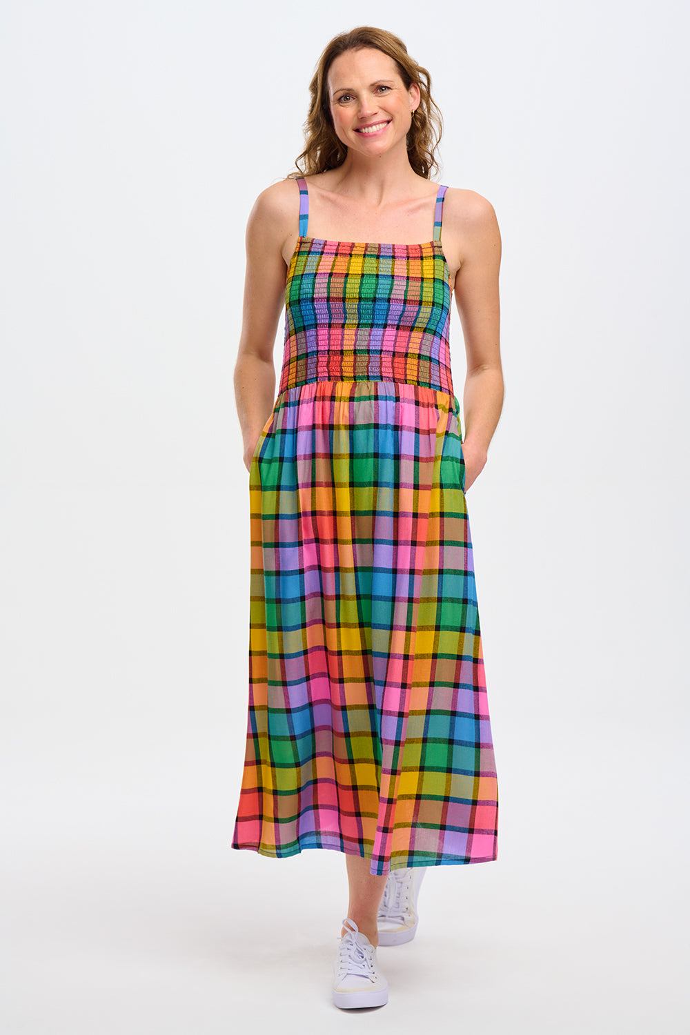 A woman wearing a multicolored checkered midi sundress with a shirred bodice and thin straps, in a rainbow check pattern.