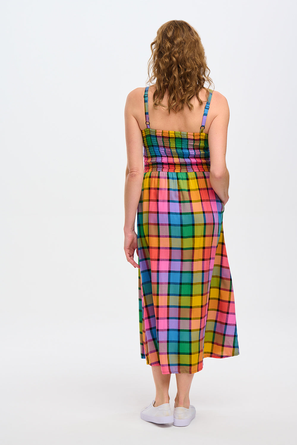 A woman wearing a multicolored checkered midi sundress with a shirred bodice and thin straps, in a rainbow check pattern.