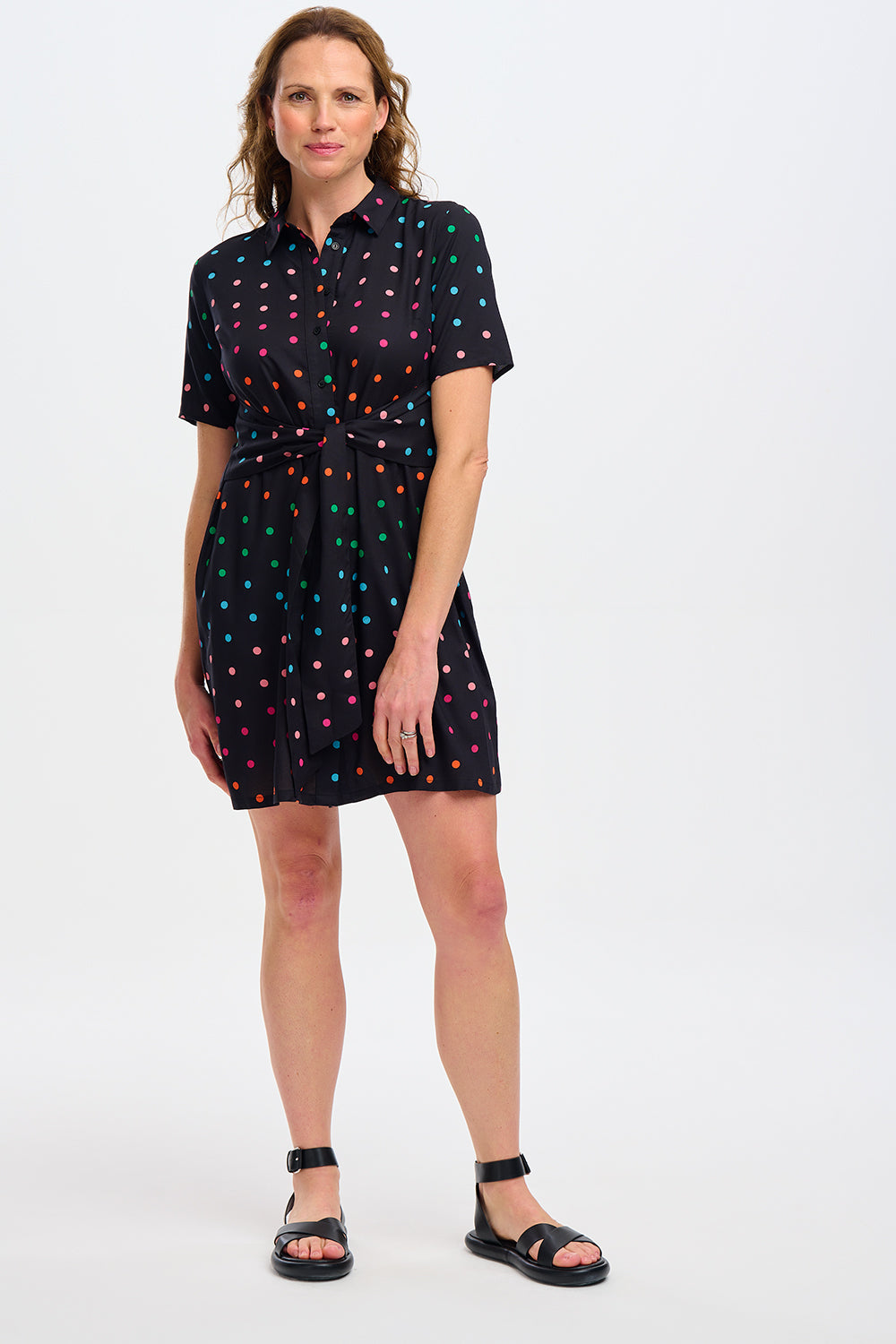 Woman wearing a black dress with colorful polka dots against a white wall