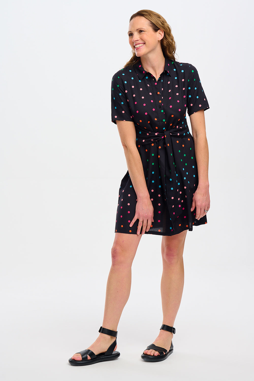 A black dress with colorful polka dots against a stone wall.