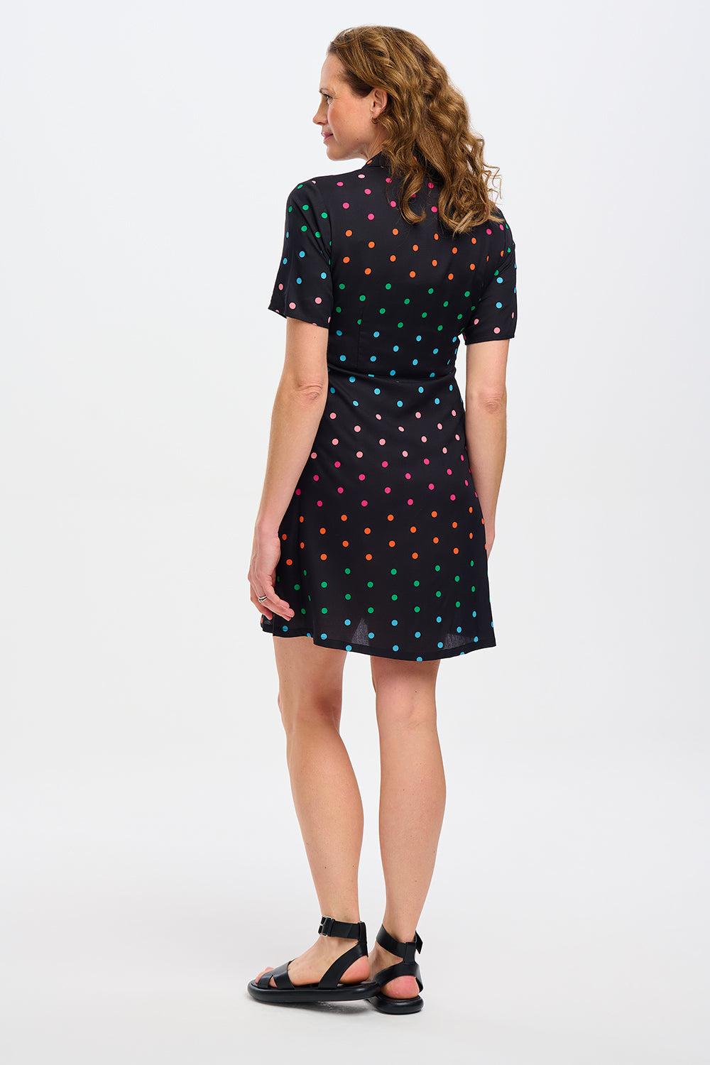 Woman wearing a black dress with colorful polka dots against a white wall