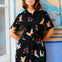 Woman wearing a black dress with colorful bird patterns in front of a colorful mural.