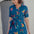 A model wearing a teal shirt dress with a Rainbow Parrot print, featuring a button-up front, short sleeves, and a tie-front belt.