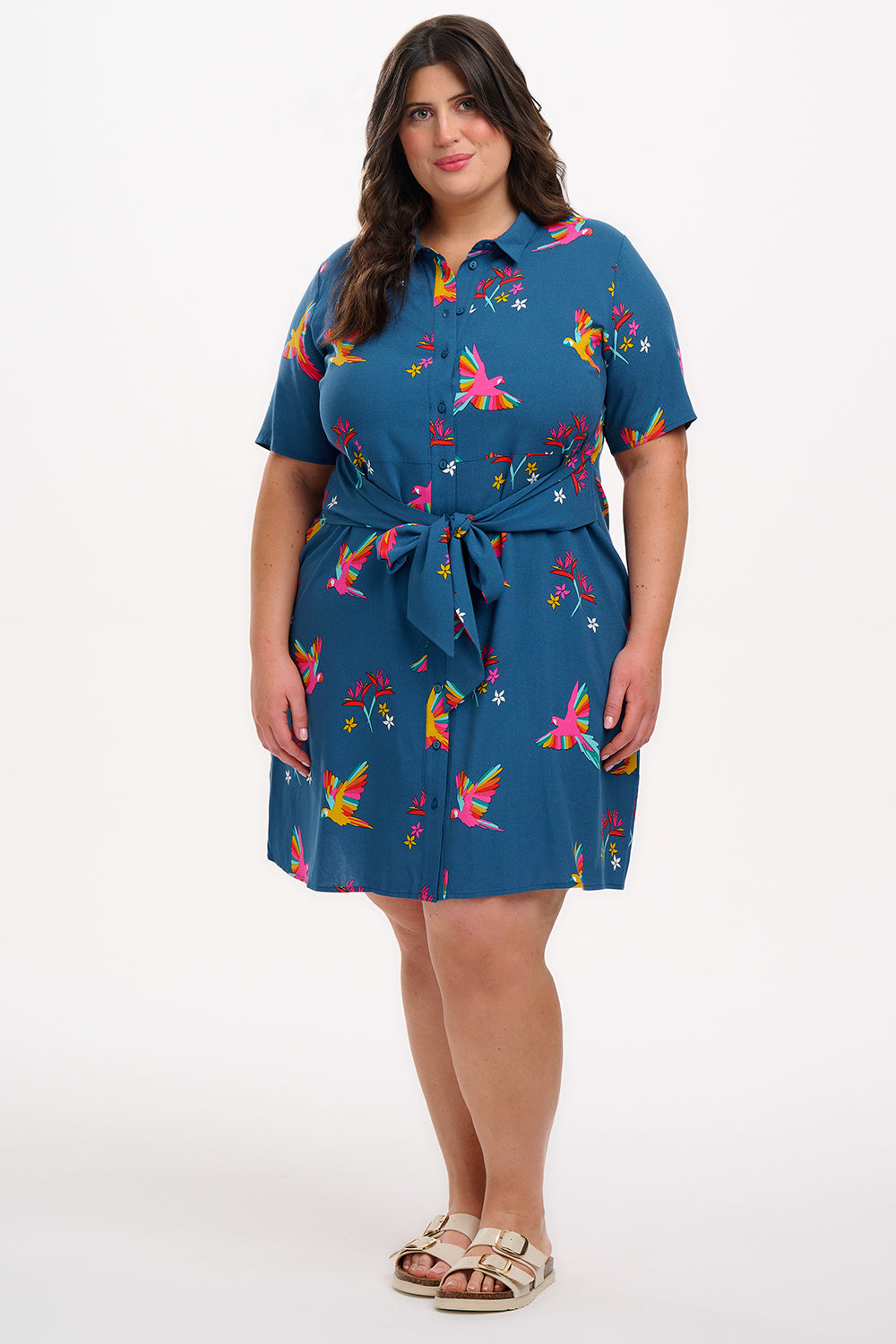 A model wearing a teal shirt dress with a Rainbow Parrots print, featuring short sleeves and a tie-front belt.