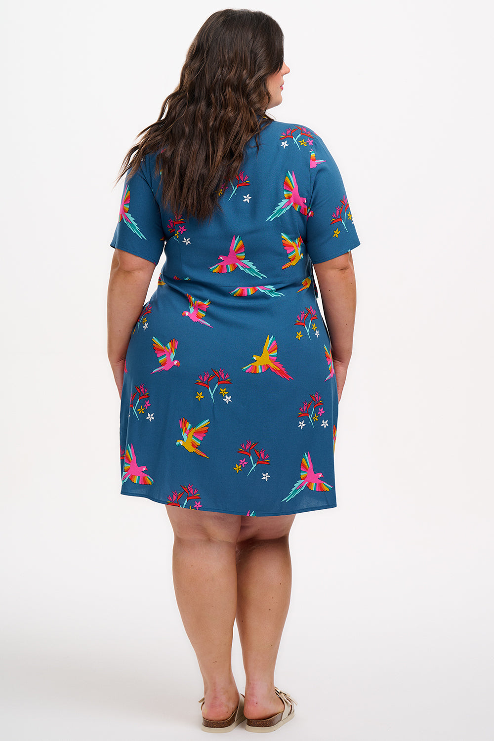 A model wearing a teal shirt dress with a Rainbow Parrots print, featuring short sleeves and a tie-front belt.