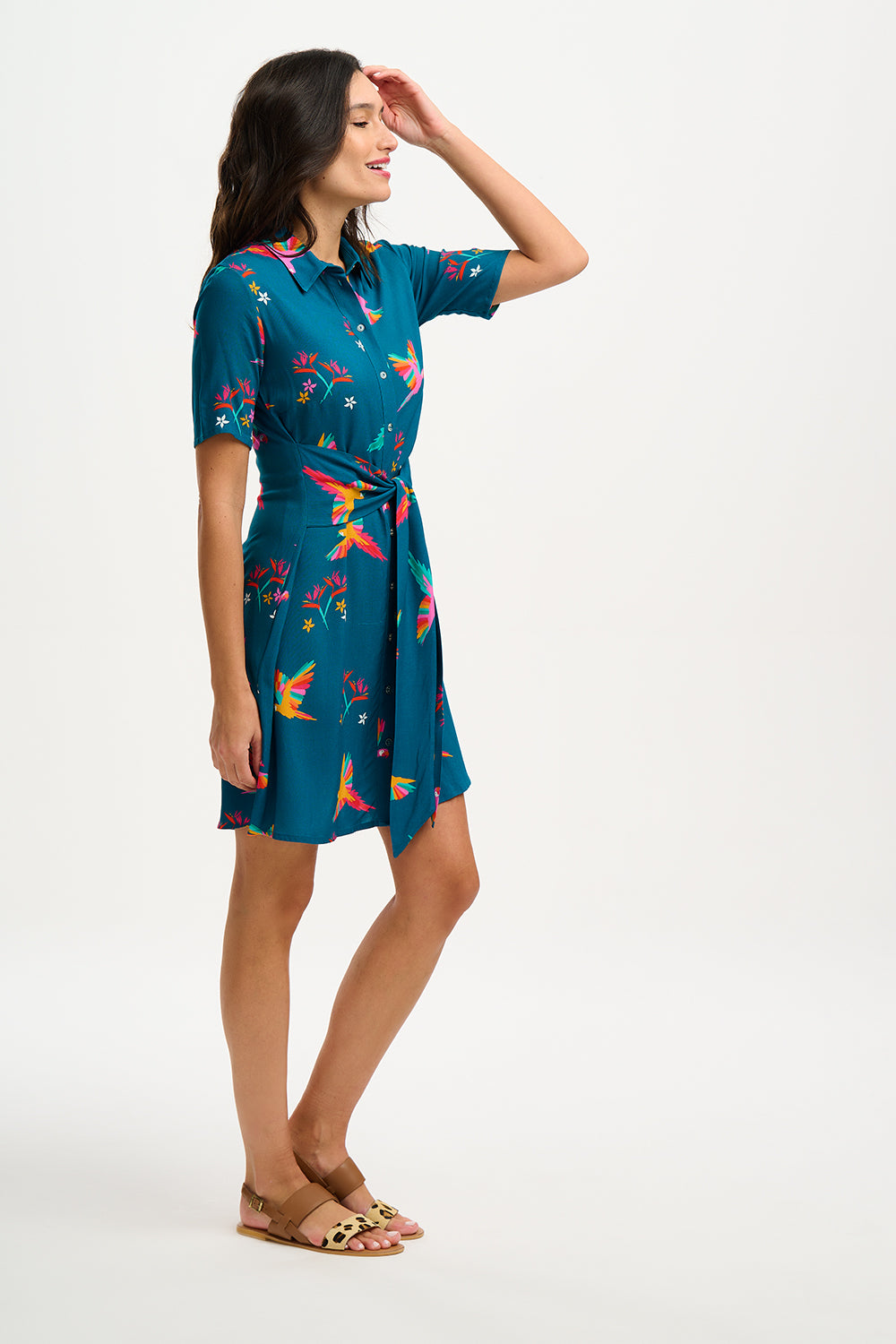 A model wearing a teal shirt dress with a Rainbow Parrots print, featuring short sleeves and a tie-front belt.