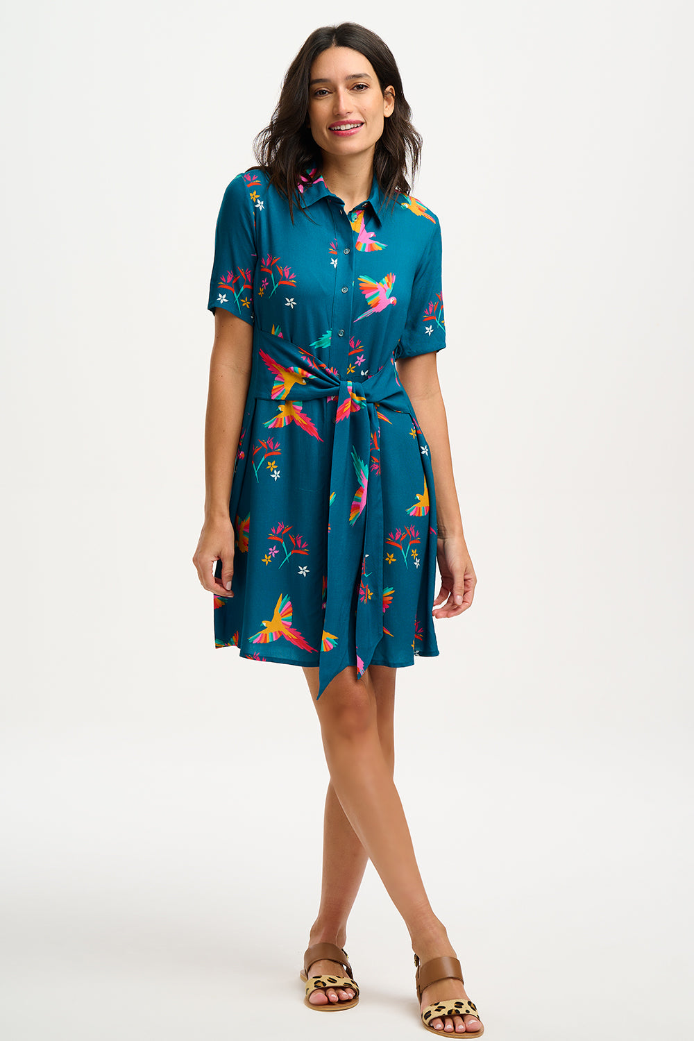 A model wearing a teal shirt dress with a Rainbow Parrots print, featuring short sleeves and a tie-front belt.