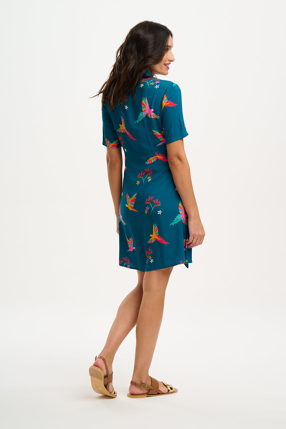 A model wearing a teal shirt dress with a Rainbow Parrots print, featuring short sleeves and a tie-front belt.