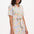 A model wearing an off-white shirt dress with a mottled leopard print, featuring a button-up front, short sleeves, and a tie-front belt.