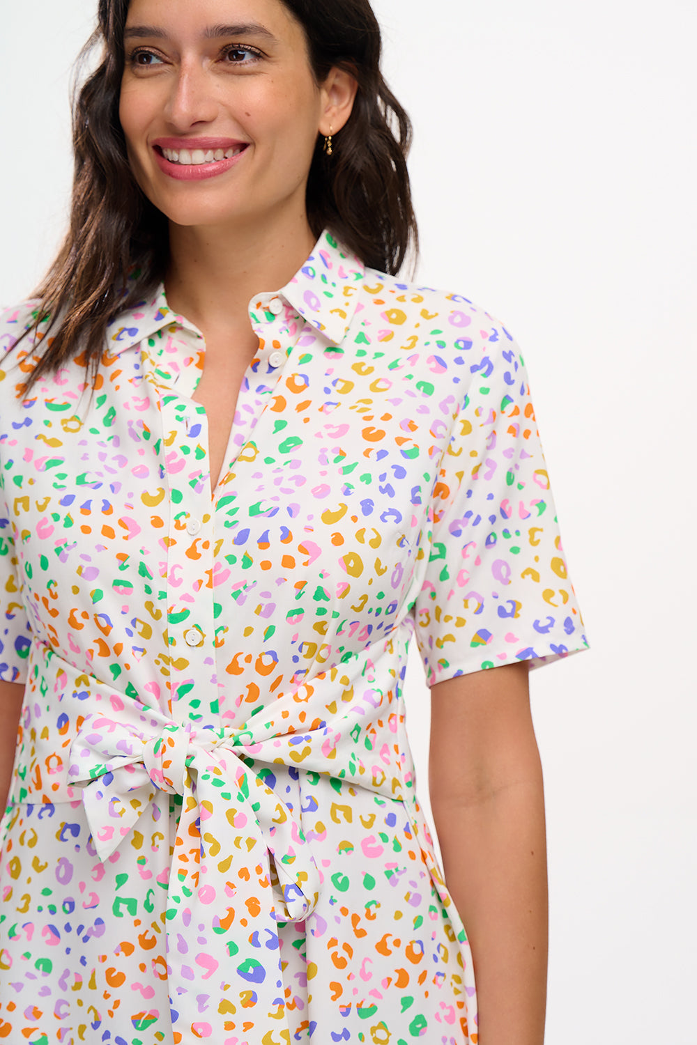 A model wearing an off-white shirt dress with a mottled leopard print, featuring a button-up front, short sleeves, and a tie-front belt.