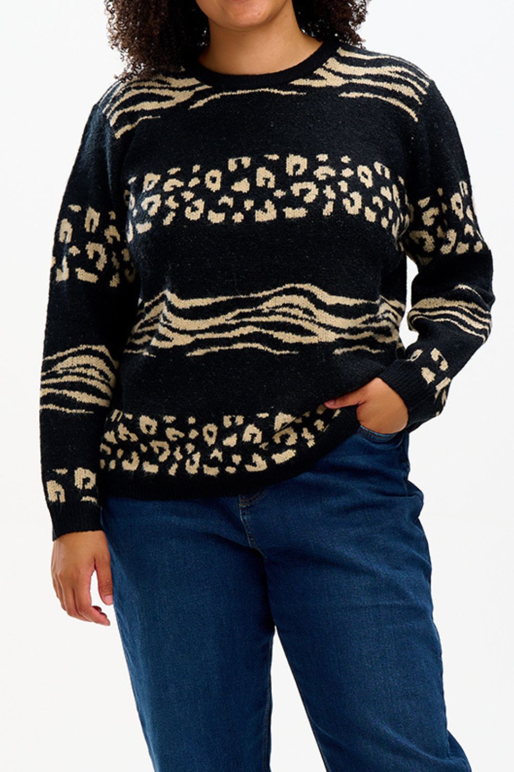 Person wearing a black sweater with beige animal print pattern and blue jeans on a white background