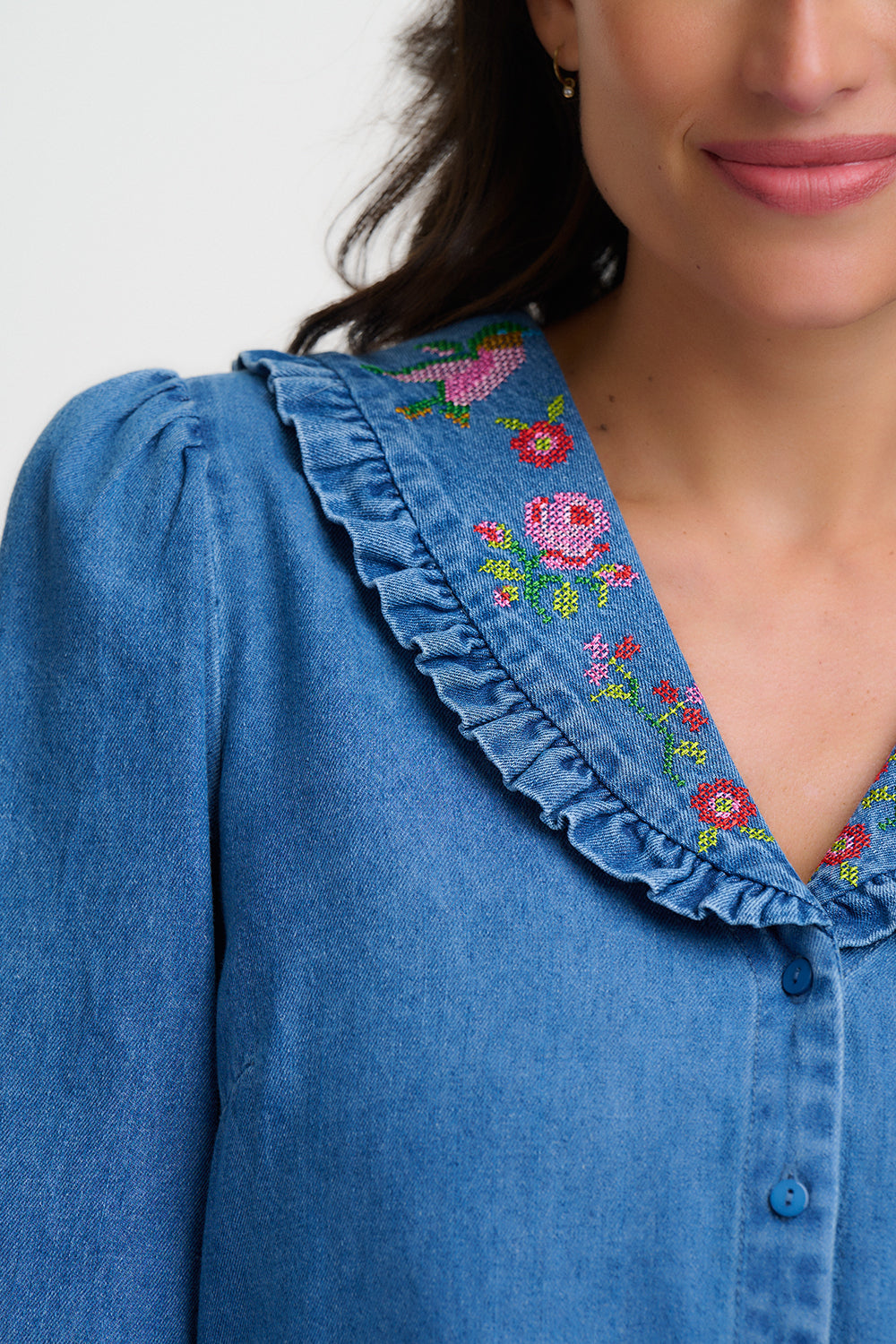 Close-up of a blue denim shirt with floral embroidery on a plain background