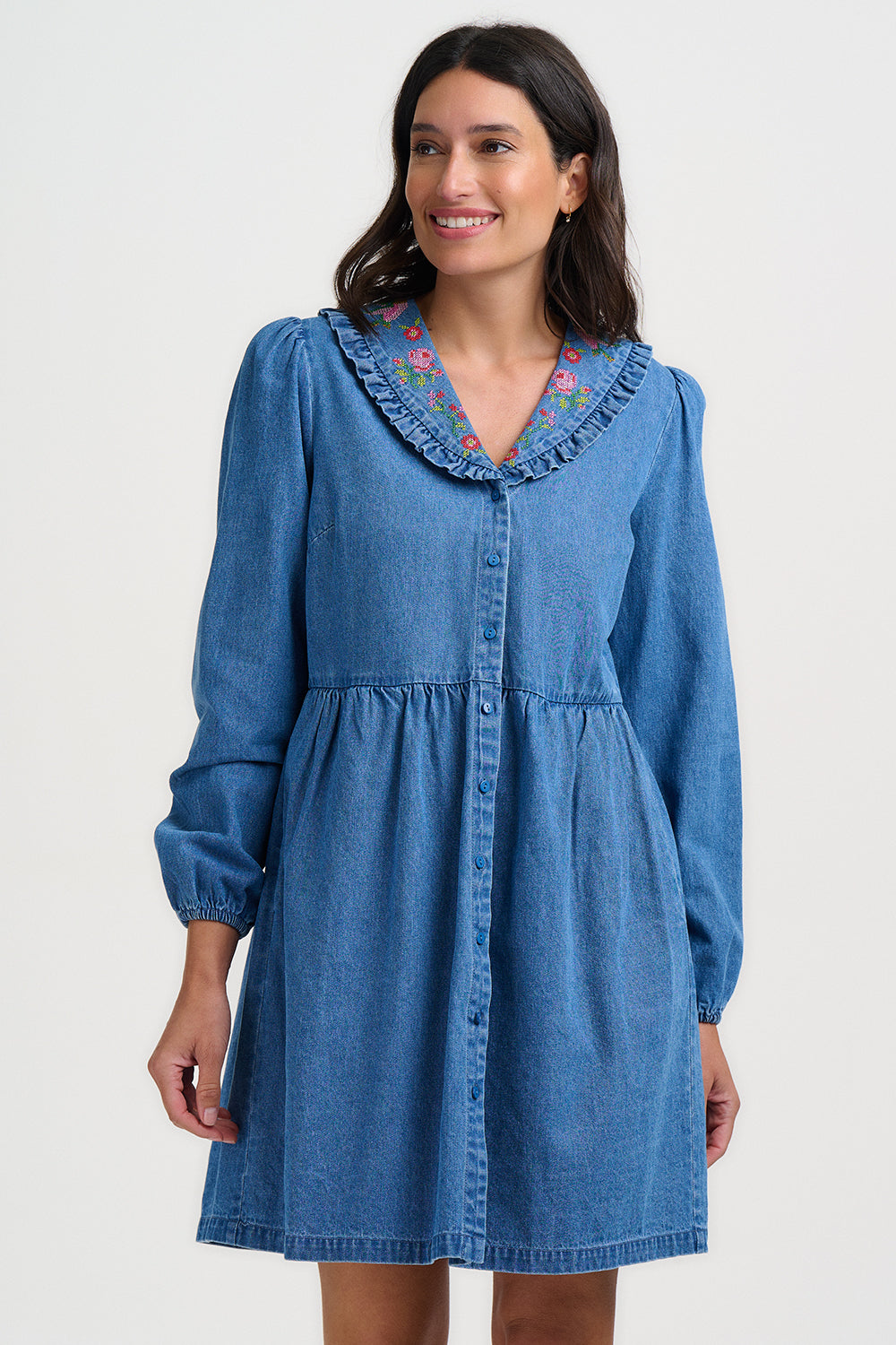 Woman wearing a blue denim dress with floral embroidery on a white background
