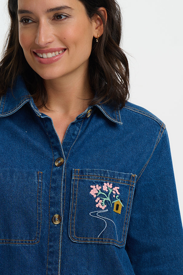 Woman wearing a blue denim jacket with floral embroidery on a white background