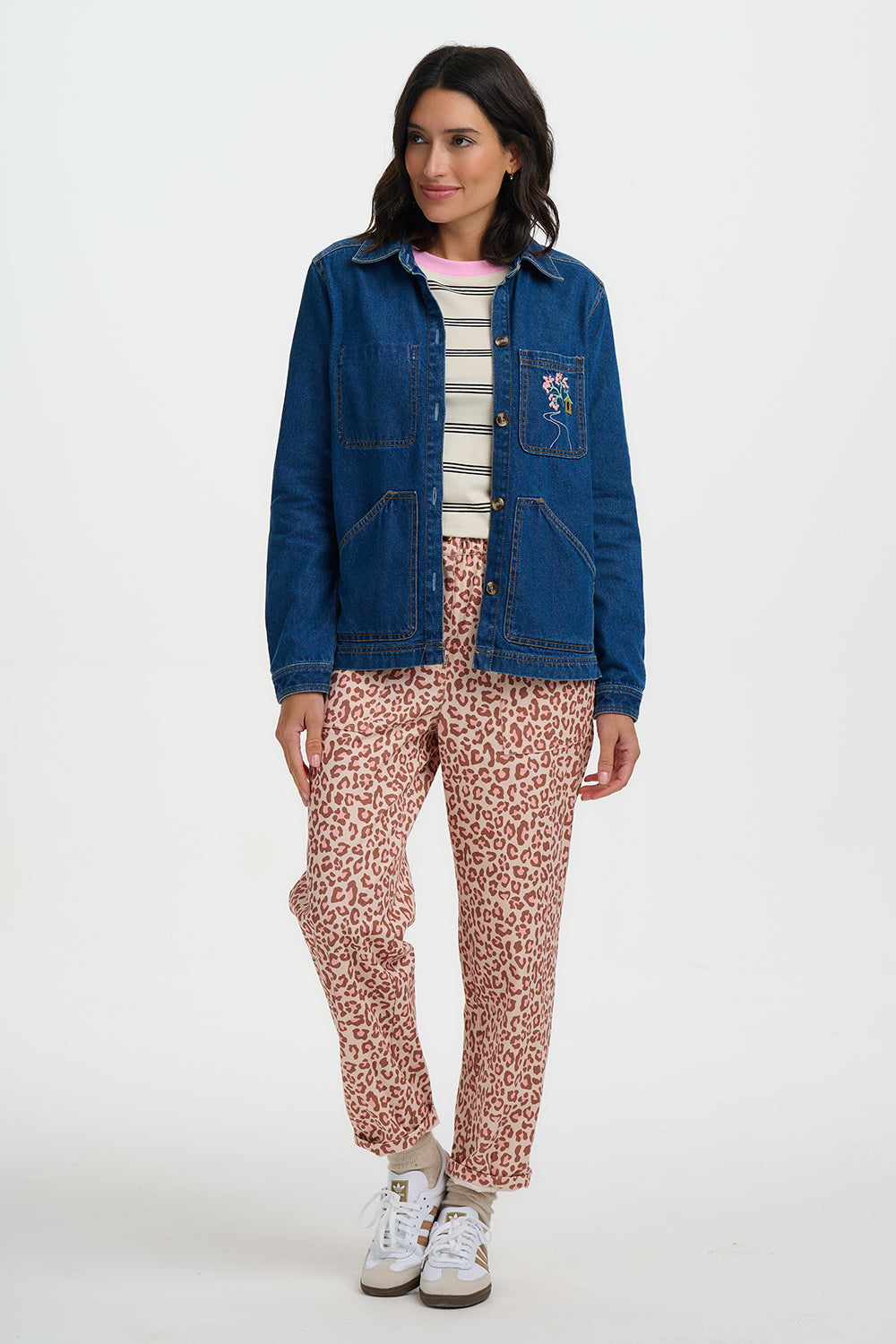 Woman wearing a blue denim jacket, striped shirt, and pink leopard print pants on a white background
