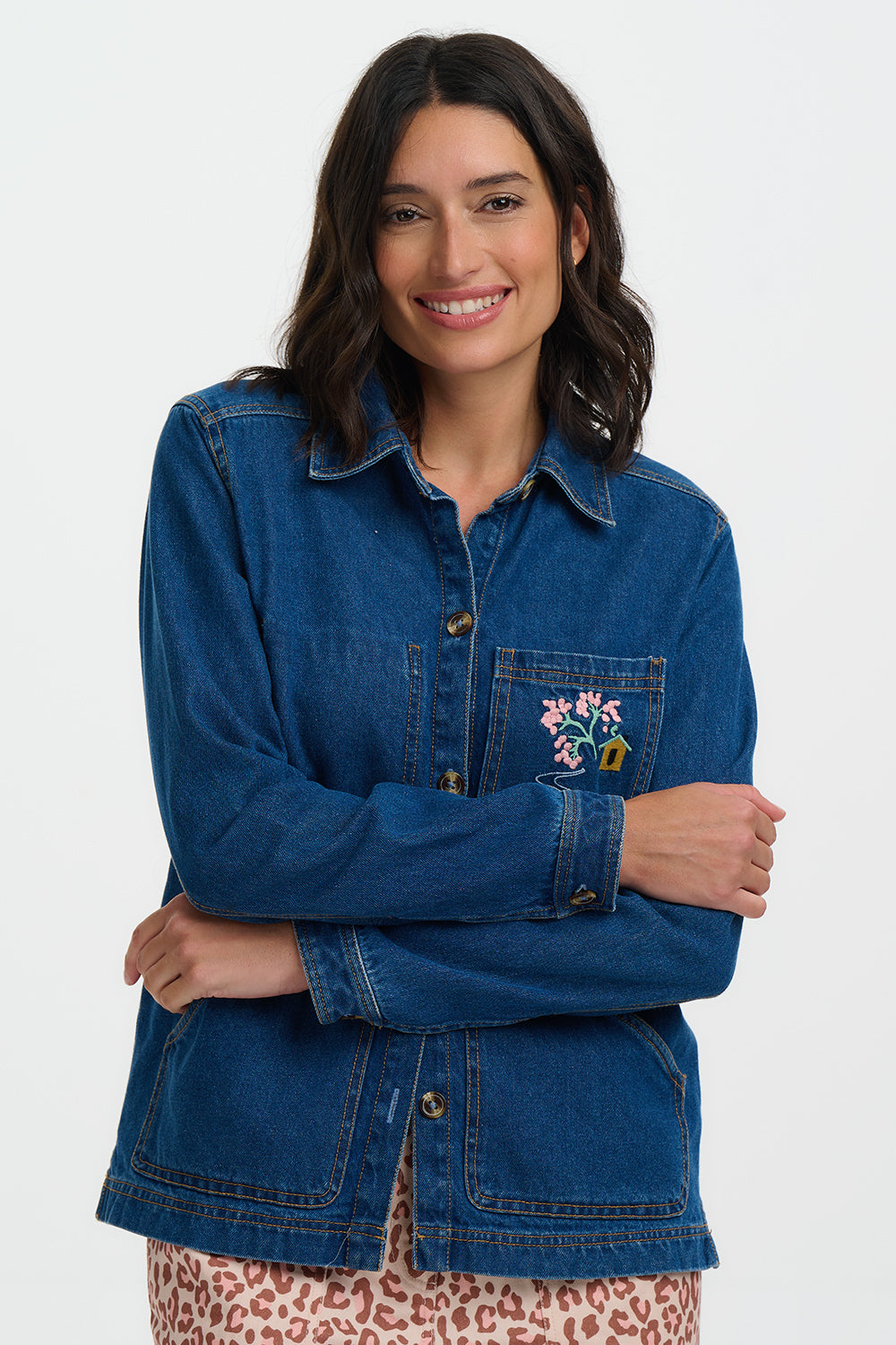 Woman wearing a blue denim jacket with floral embroidery on a white background