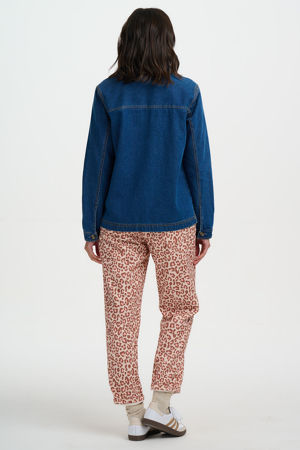 Person wearing a blue denim jacket and patterned pants on a white background