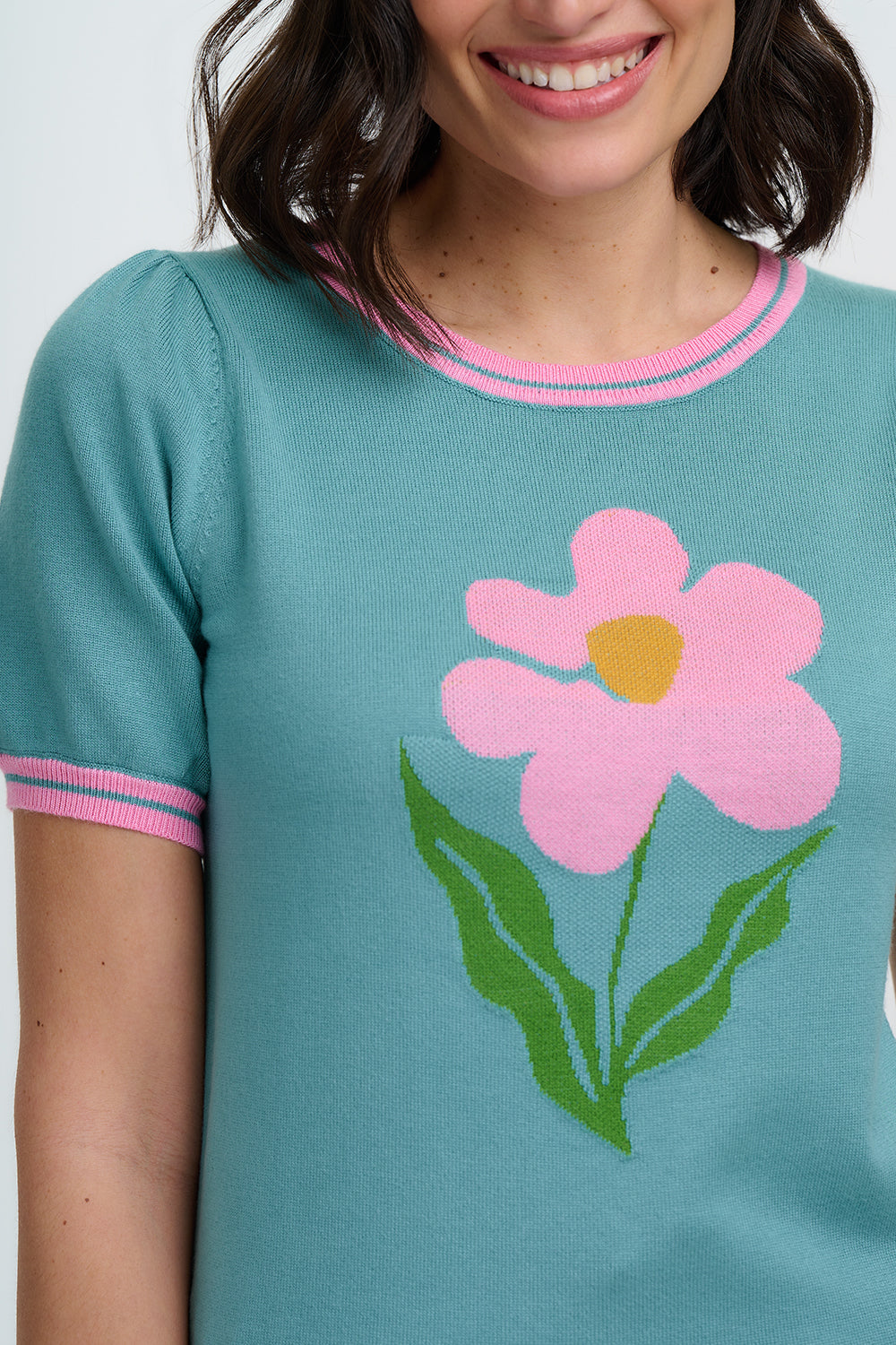 Person wearing a teal sweater with a pink flower design on a white background
