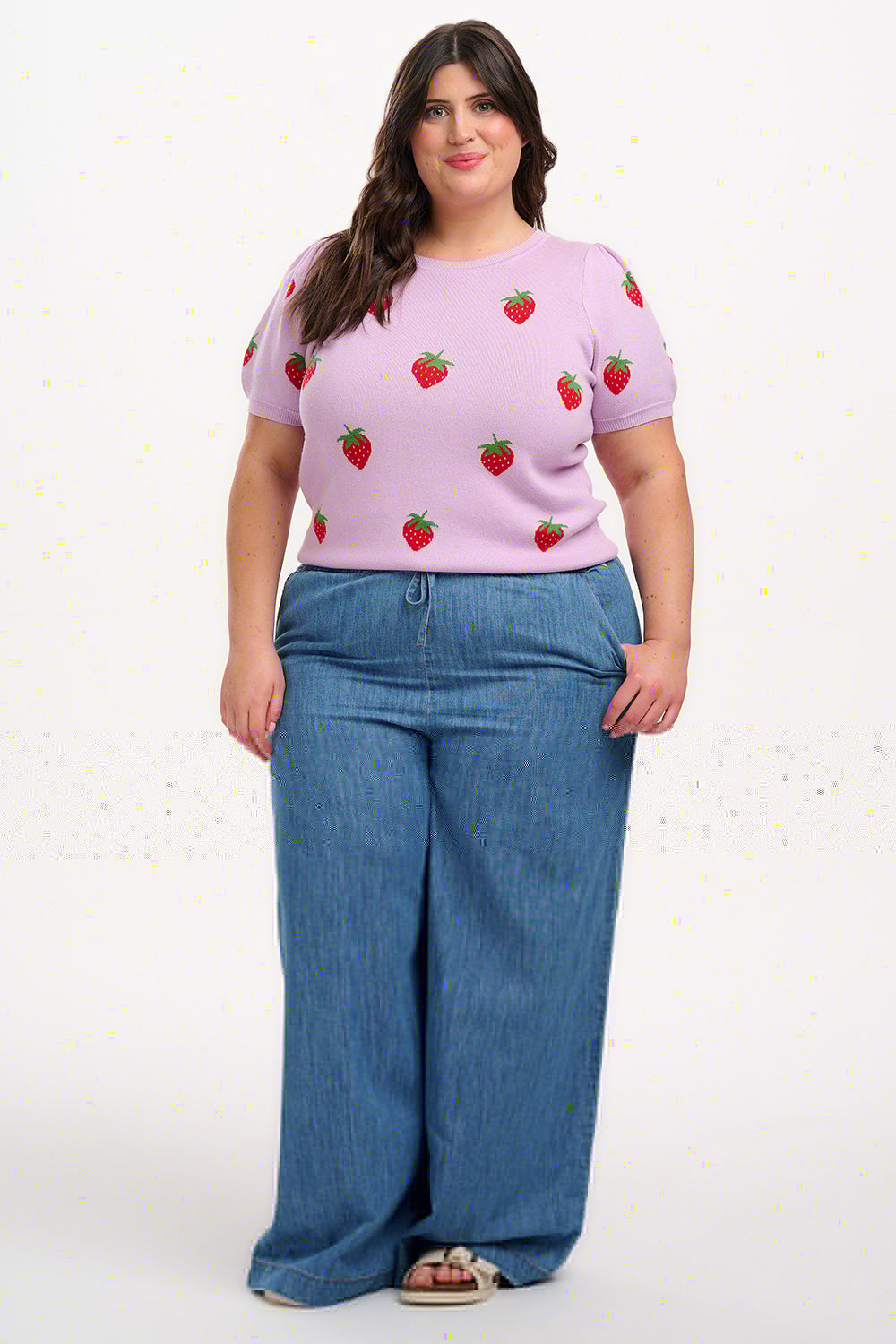 A woman wearing a lilac-colored knit top with a pattern of vibrant strawberries.