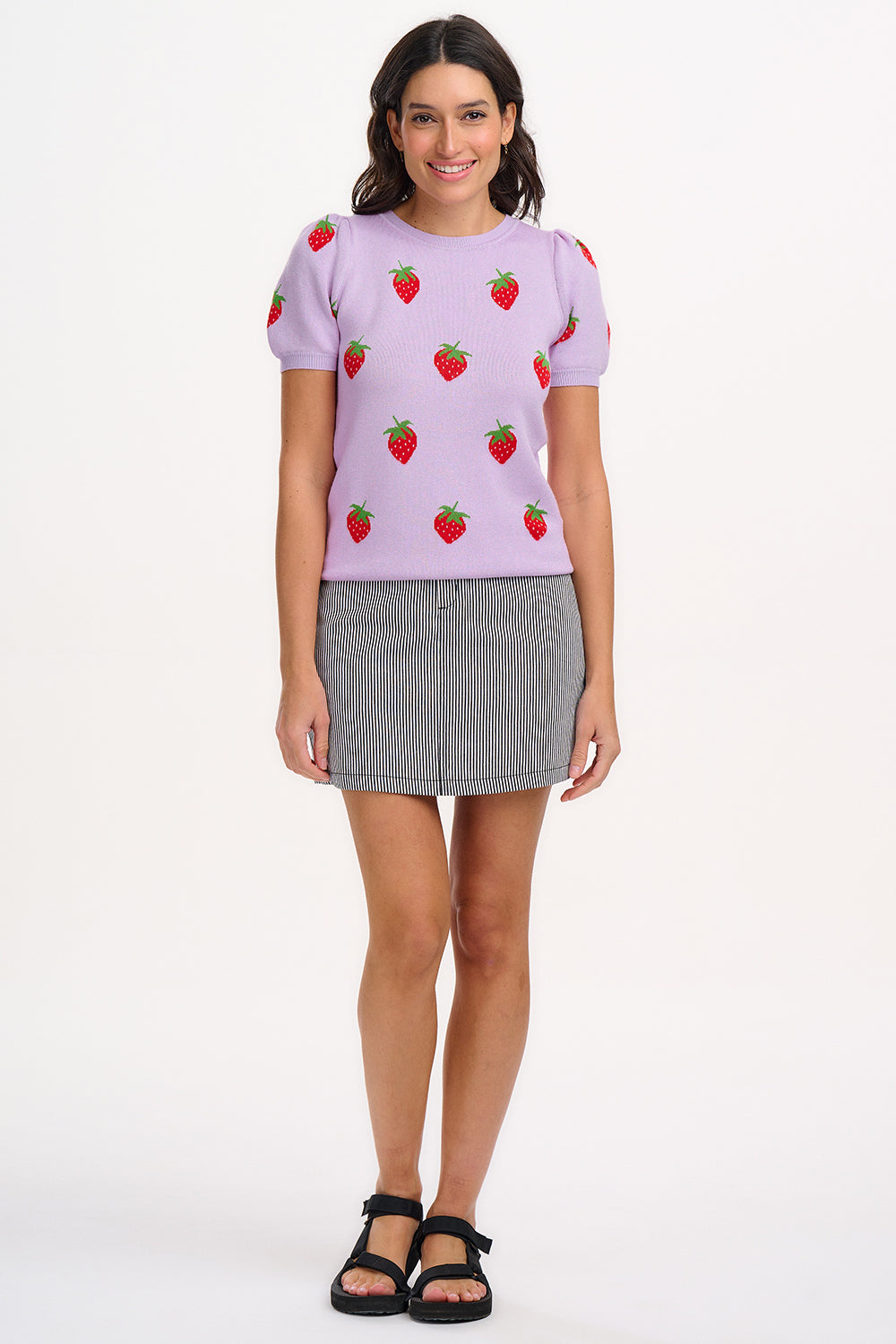 A woman wearing a lilac-colored knit top with a pattern of vibrant strawberries.