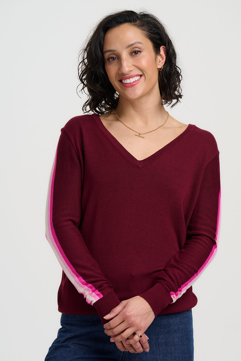 Woman wearing a burgundy sweater with pink and white trim on a plain background
