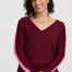 Woman wearing a burgundy sweater with pink and white trim on a plain background