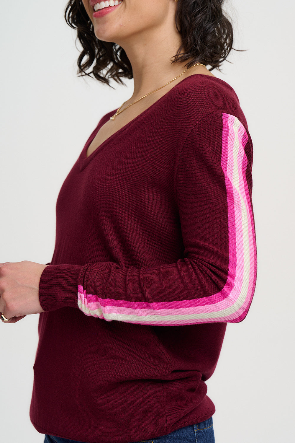 Maroon sweater with pink and white striped sleeves worn by a person on a white background