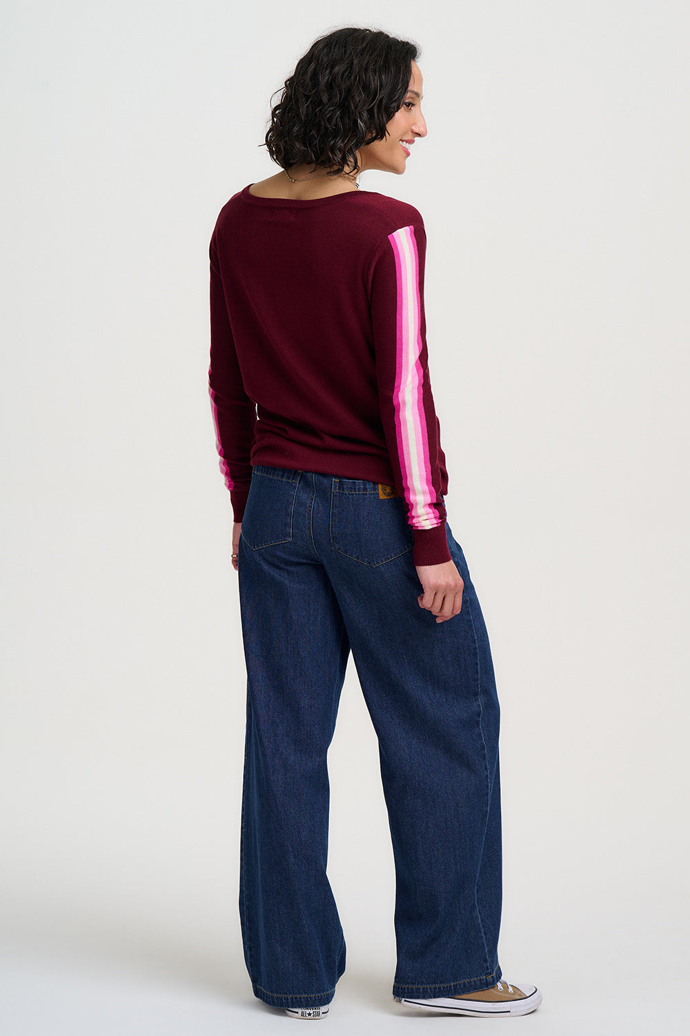 Person wearing a burgundy sweater with pink stripes and blue jeans on a white background