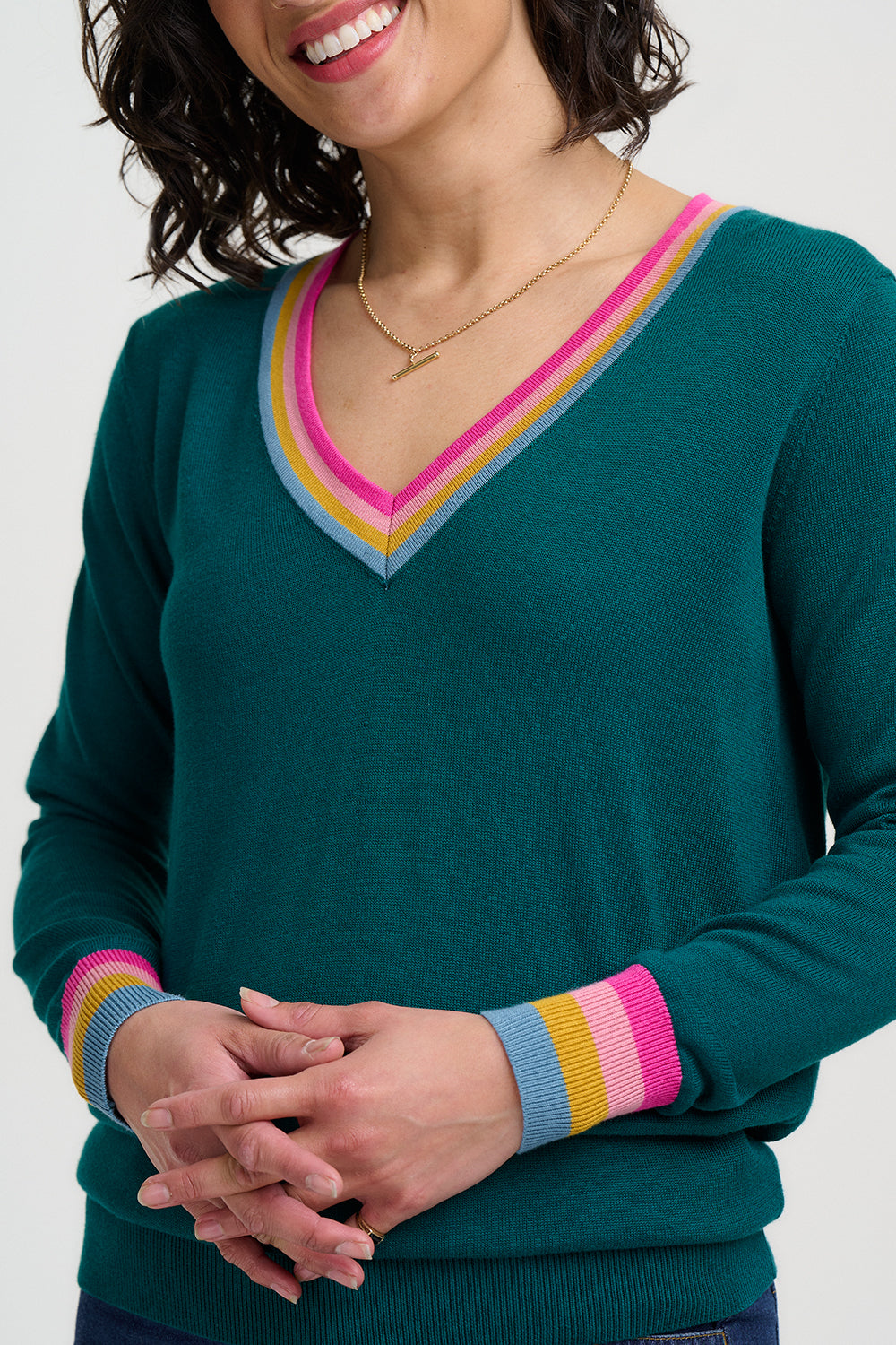 Woman wearing a teal sweater with colorful cuffs and neckline on a white background