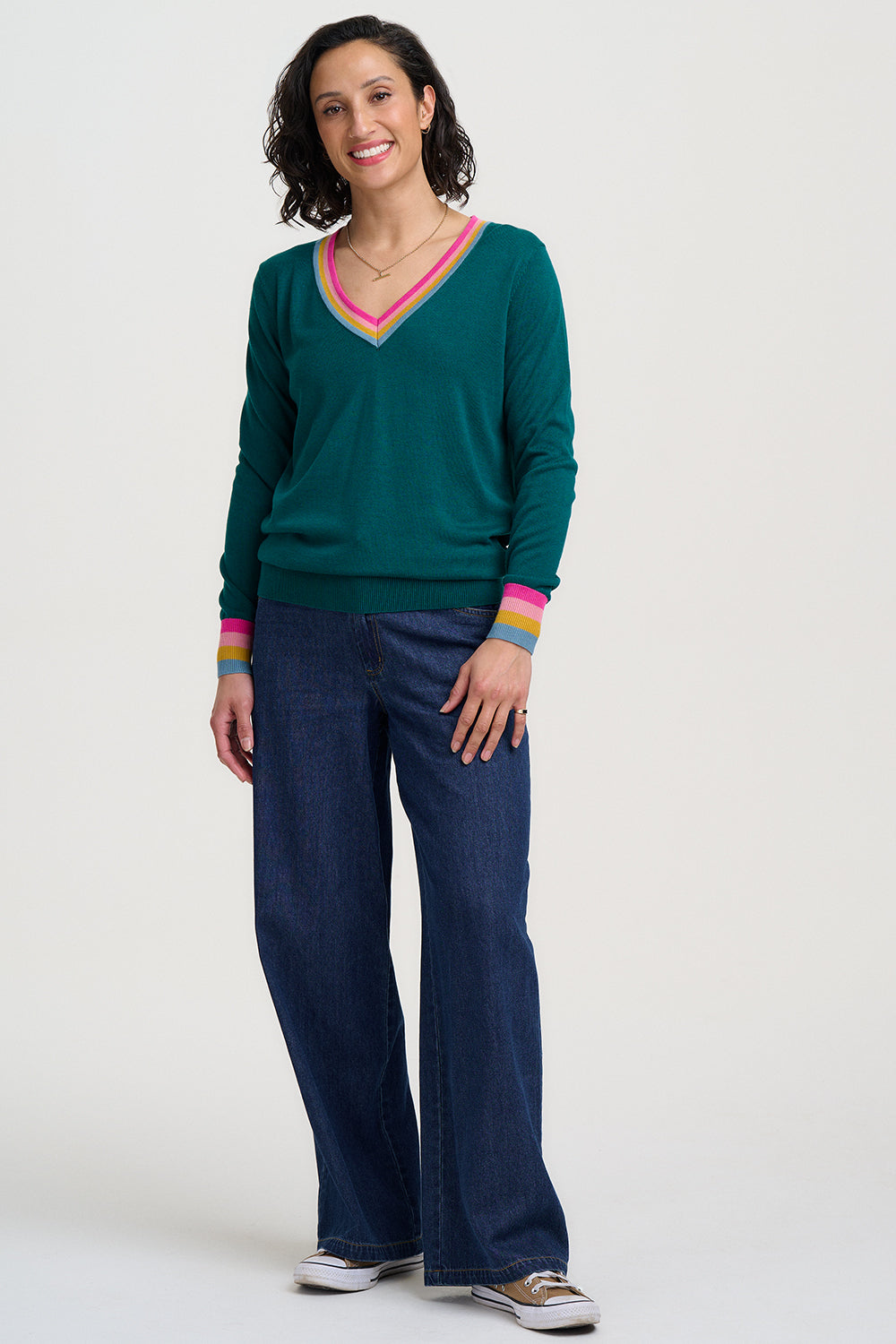 Woman wearing a green sweater with colorful trim and blue pants on a white background