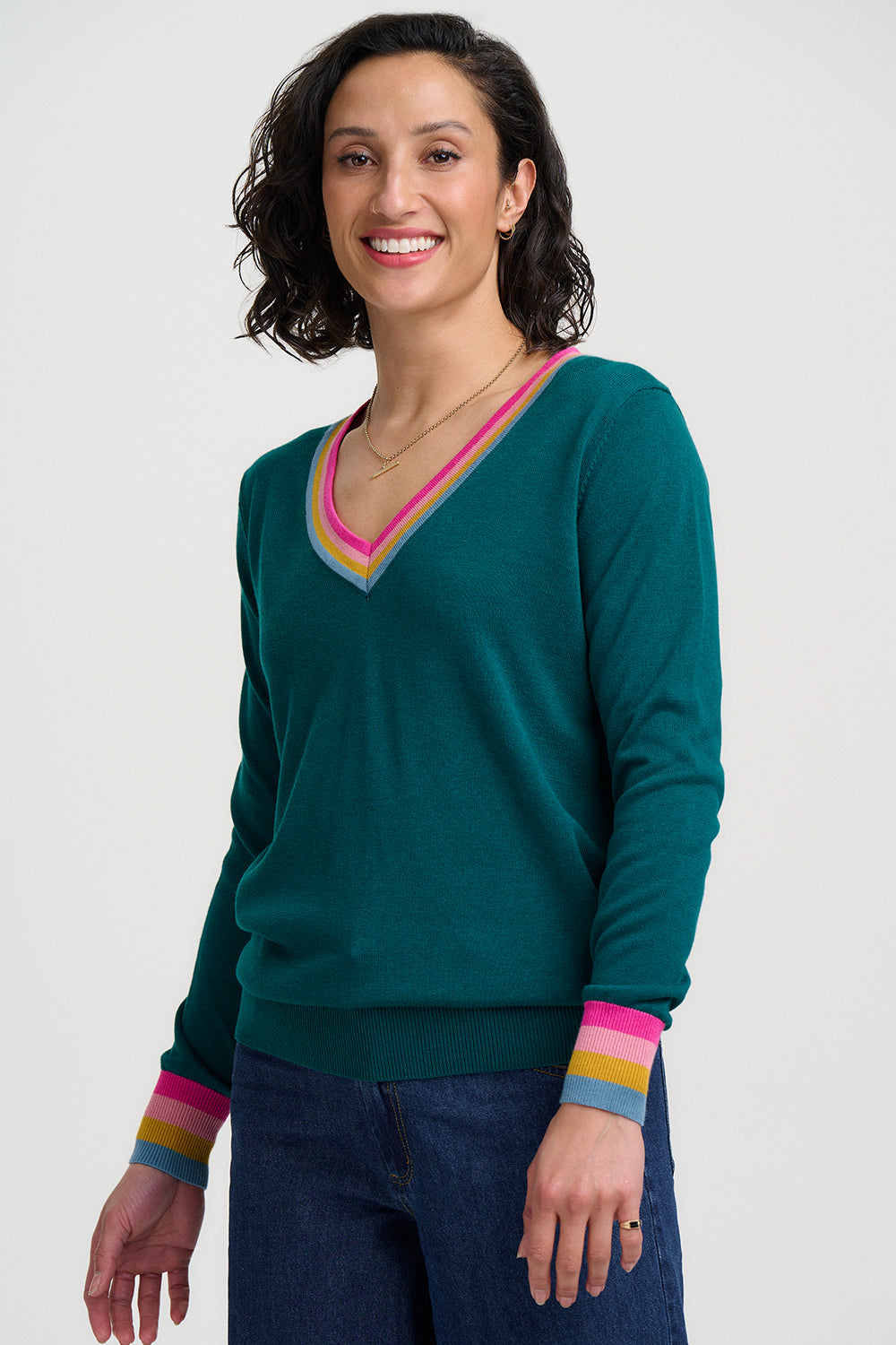 Woman wearing a teal sweater with colorful cuffs and hem on a white background