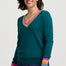 Woman wearing a teal sweater with colorful cuffs and hem on a white background