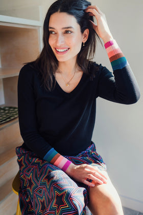 Sugarhill Brighton model wearing a black V-neck jumper with multicoloured stripe cuffs, paired with blue jeans.