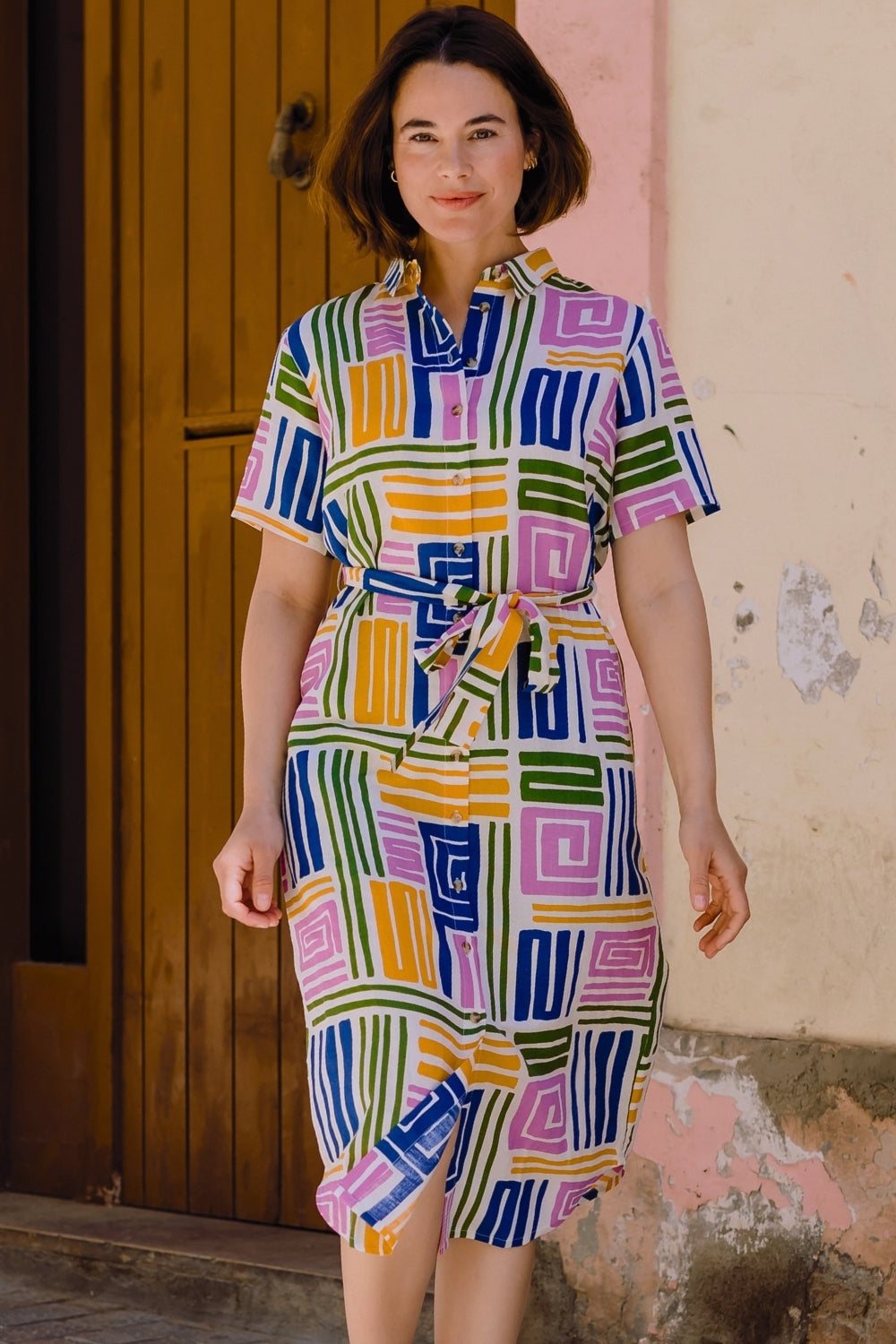 Woman wearing a colorful geometric patterned dress standing against a textured wall.