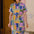 Woman wearing a colorful geometric patterned dress standing against a textured wall.