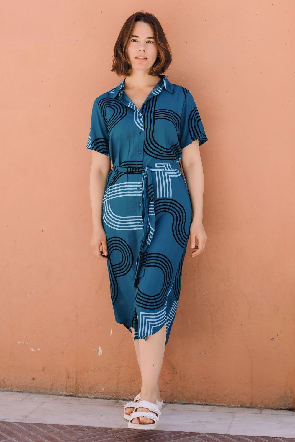 Woman wearing a blue patterned dress against a brown wall