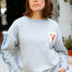 Person wearing a light gray sweatshirt with a patch and a blue cap outdoors.