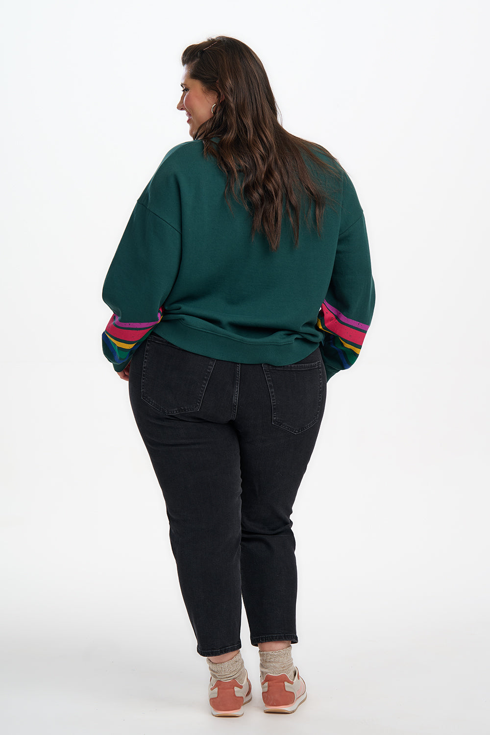 Person wearing a green sweatshirt with colorful sleeves and black pants on a white background