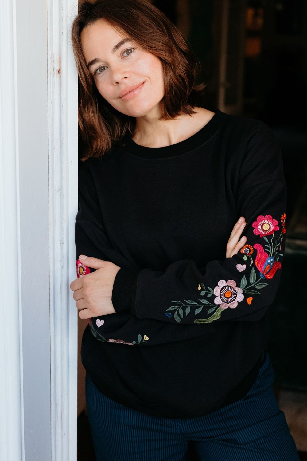 Woman wearing a black sweatshirt with floral designs and teal pants on a white background