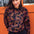 A woman wearing a black sweatshirt with a two-tone leopard print pattern, paired with black trousers, standing in front of an orange wall.