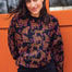 A woman wearing a black sweatshirt with a two-tone leopard print pattern, paired with black trousers, standing in front of an orange wall.
