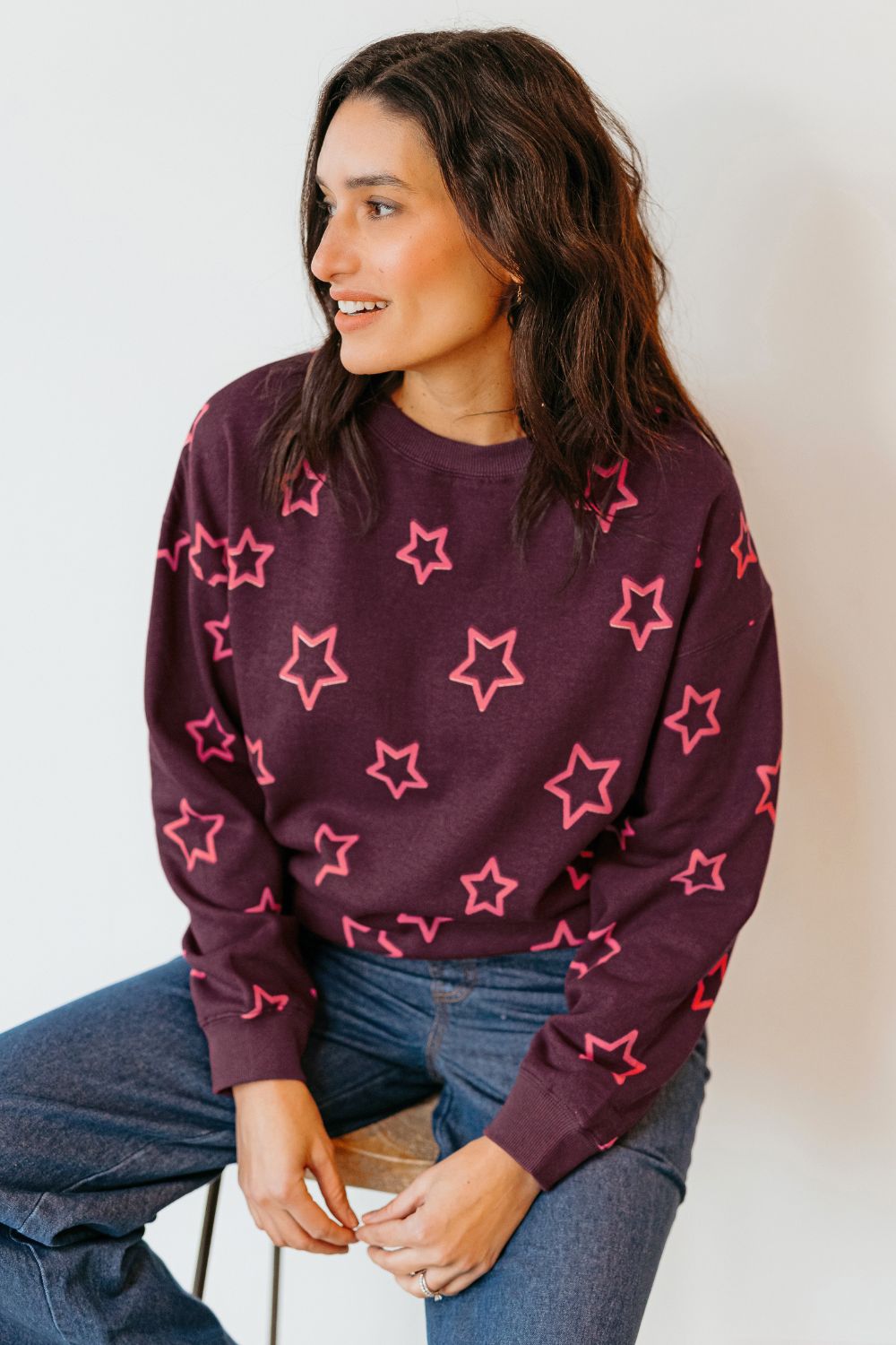 Woman wearing a dark purple sweater with pink star patterns against a plain background