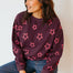 Woman wearing a dark purple sweater with pink star patterns against a plain background