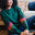 A Sugarhill Brighton model sitting on a sofa wearing a dark green crew neck sweatshirt with colourful striped sleeves.