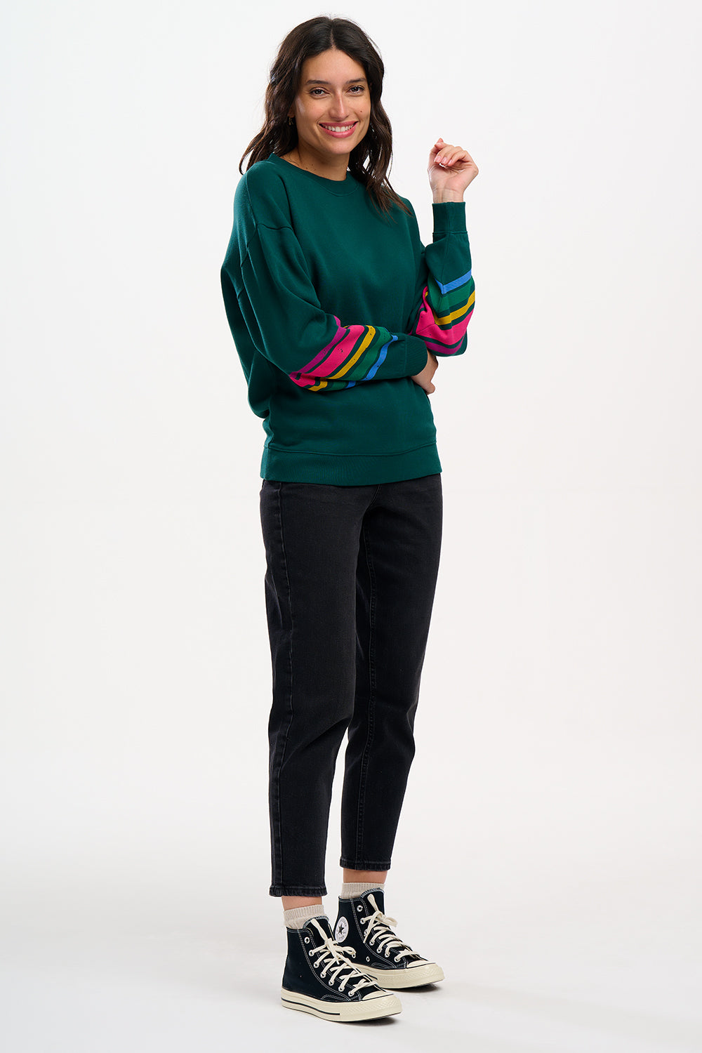 A Sugarhill Brighton model wearing a dark green crew neck sweatshirt with colourful striped sleeves.