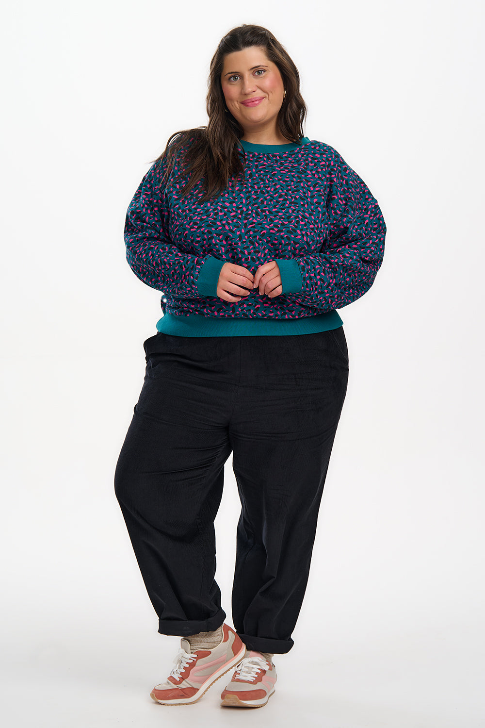 Person wearing a blue patterned sweater and black pants on a white background