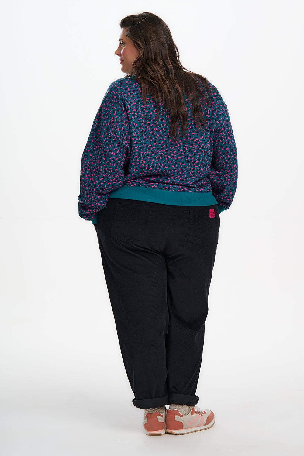 Person wearing a patterned shirt and black pants on a white background