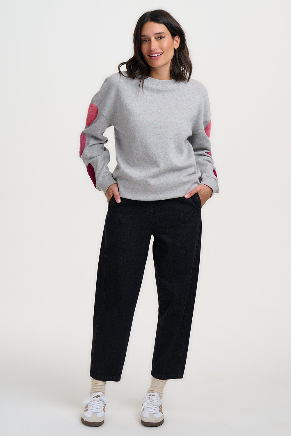 Woman wearing a gray sweater with pink accents and black pants on a white background