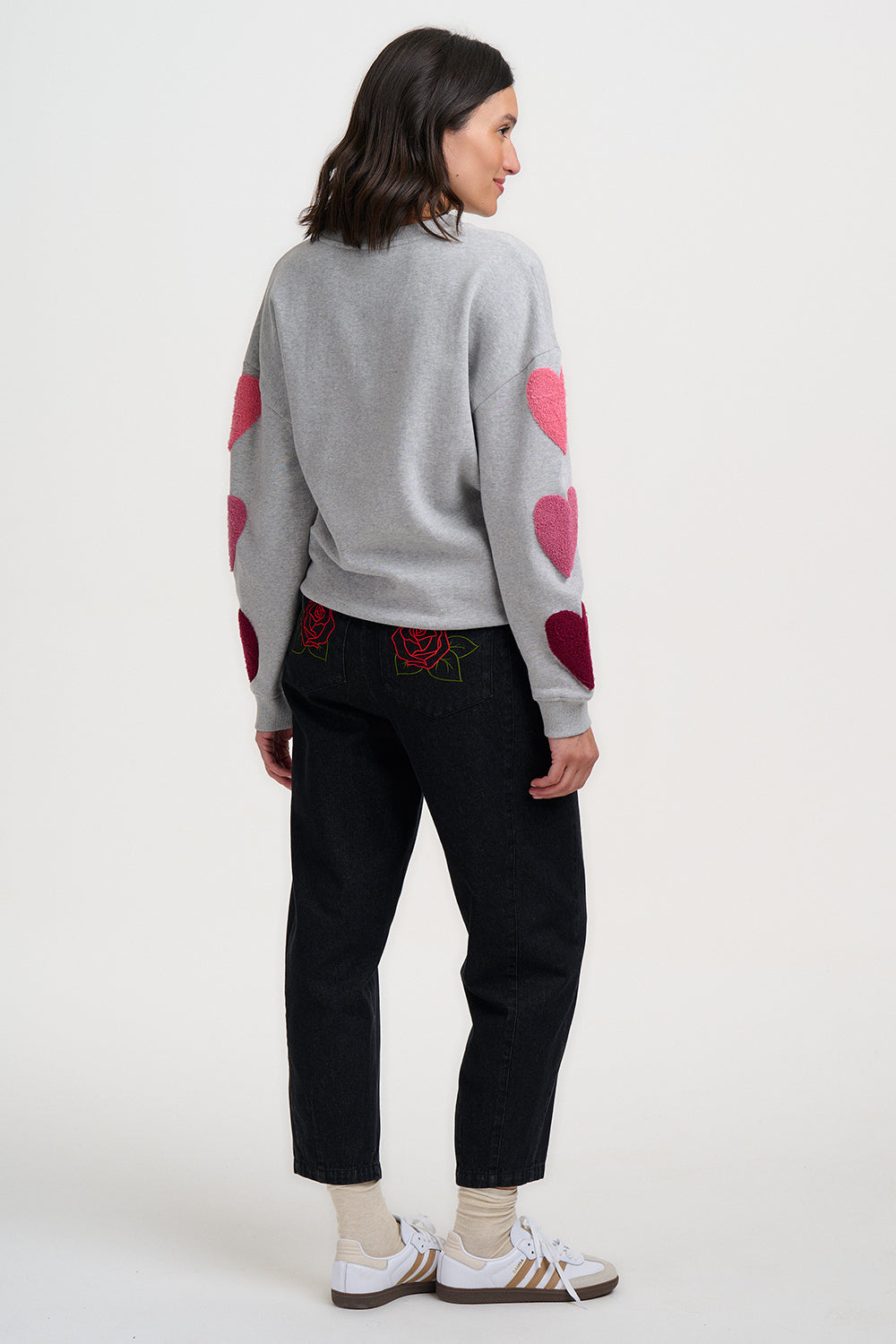 Person wearing a gray sweater with pink heart designs on a white background