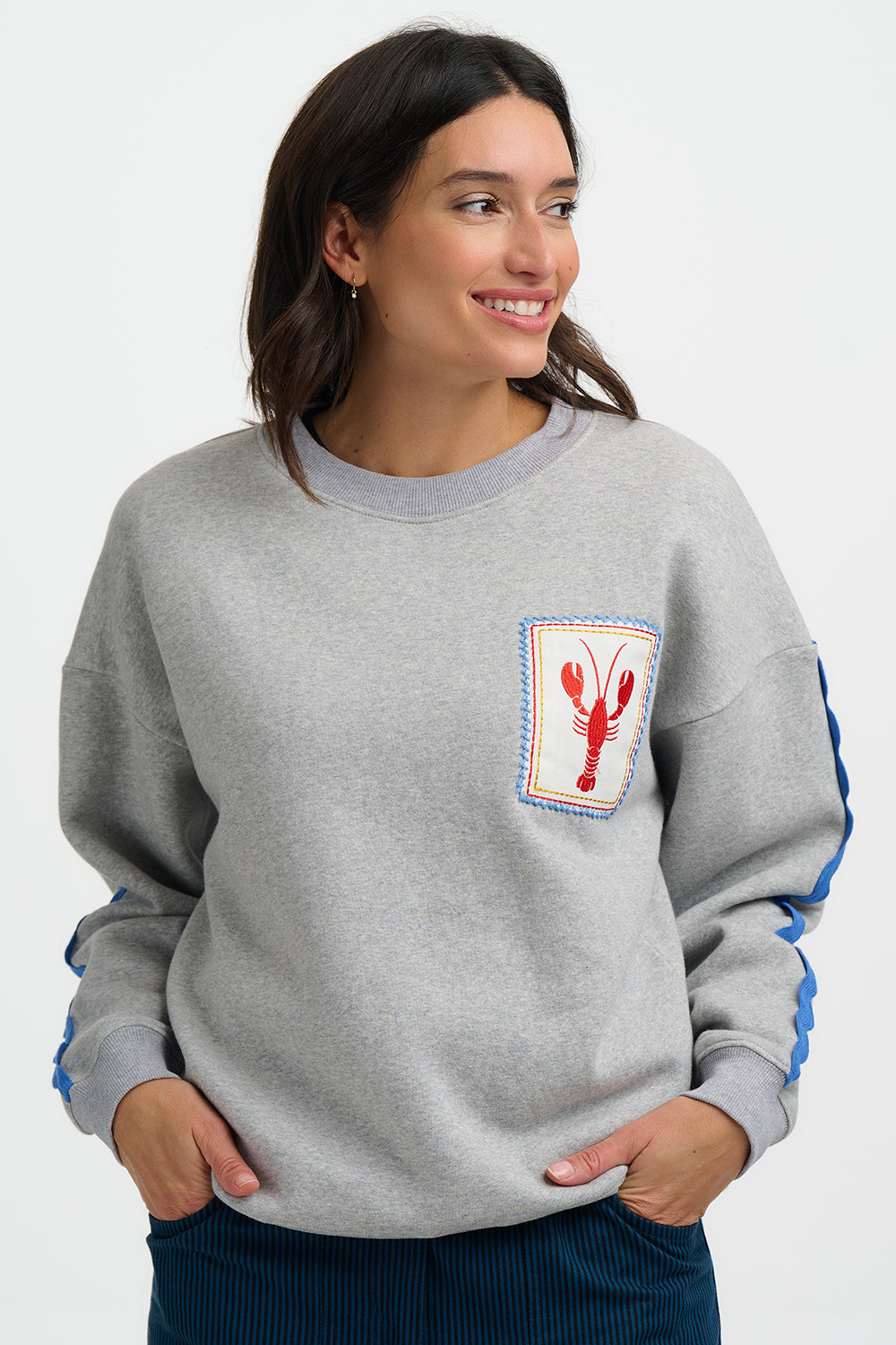 Woman wearing a gray sweatshirt with a lobster patch on a white background
